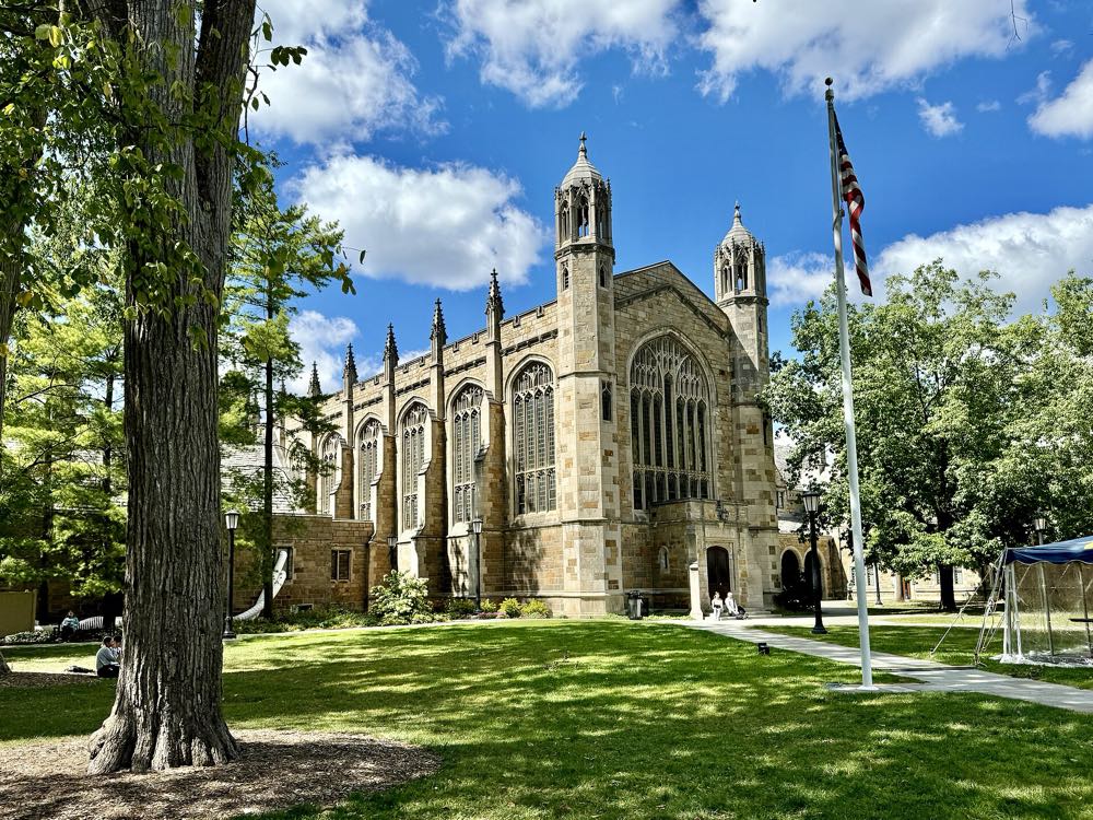 The Gothic stone Law Library of the University of Michigan Law Quadrangle with tall arched windows and pinnacles, seen across a sunny lawn under tall trees