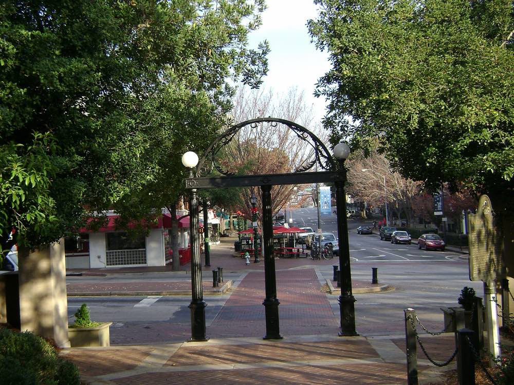 The black cast-iron Arch of the University of Georgia, with globe lamps, framing Broad Street and downtown Athens storefronts under winter trees