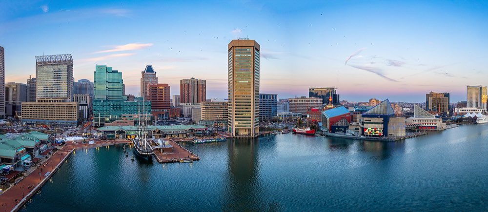 Baltimore's Inner Harbor at dusk from above, with downtown towers, the National Aquarium and a tall ship at its pier