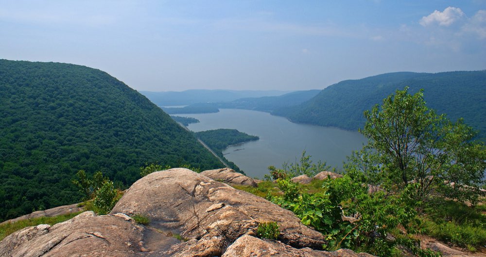 The Hudson River running south between steep green mountains, seen from a rocky ledge high on Breakneck Ridge, with Bull Hill rising on the left and a small wooded point jutting into the river below