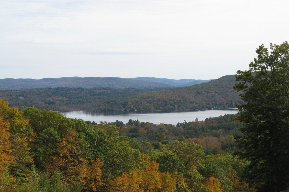 Wooded Berkshire hills in early fall color, with orange and gold trees in the foreground and the lake called Stockbridge Bowl below a line of blue ridges