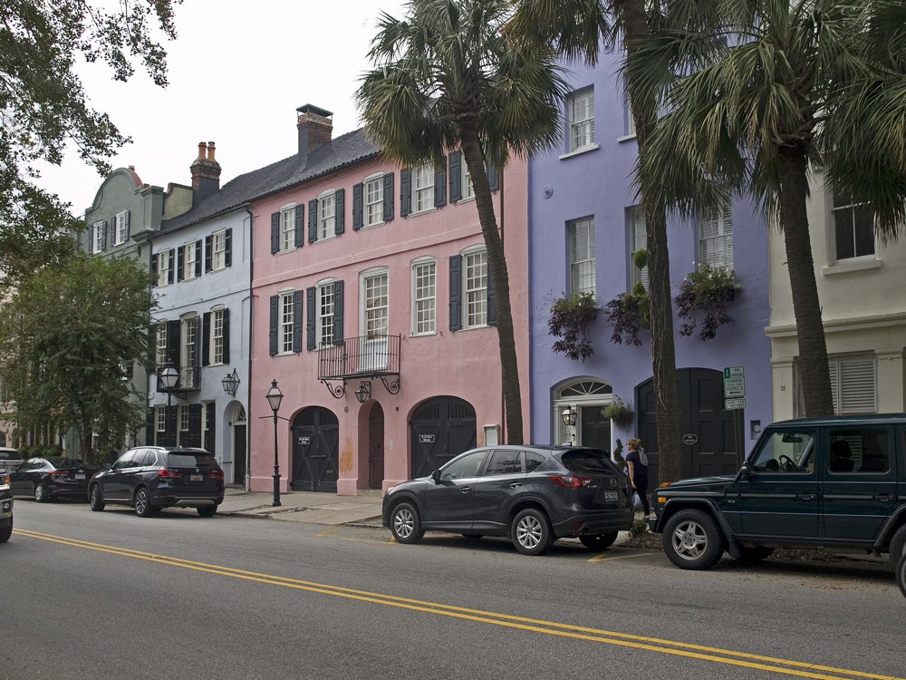 Pastel pink, blue and lavender row houses with dark shutters along East Bay Street, framed by palmetto trees under a pale sky