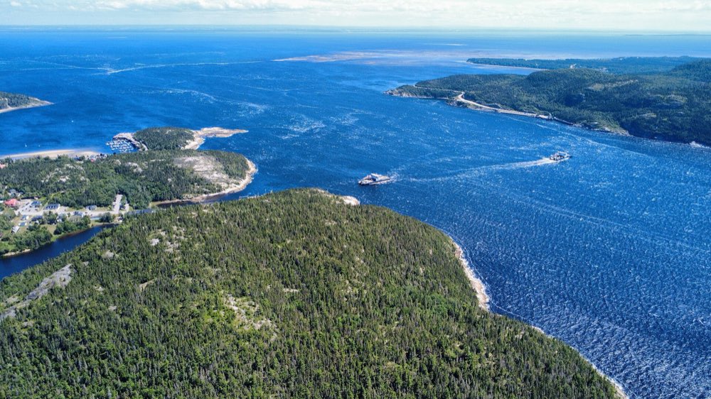 Aerial view of the mouth of the Saguenay fjord at Tadoussac: forested headlands, the deep blue river and two ferries crossing between the shores