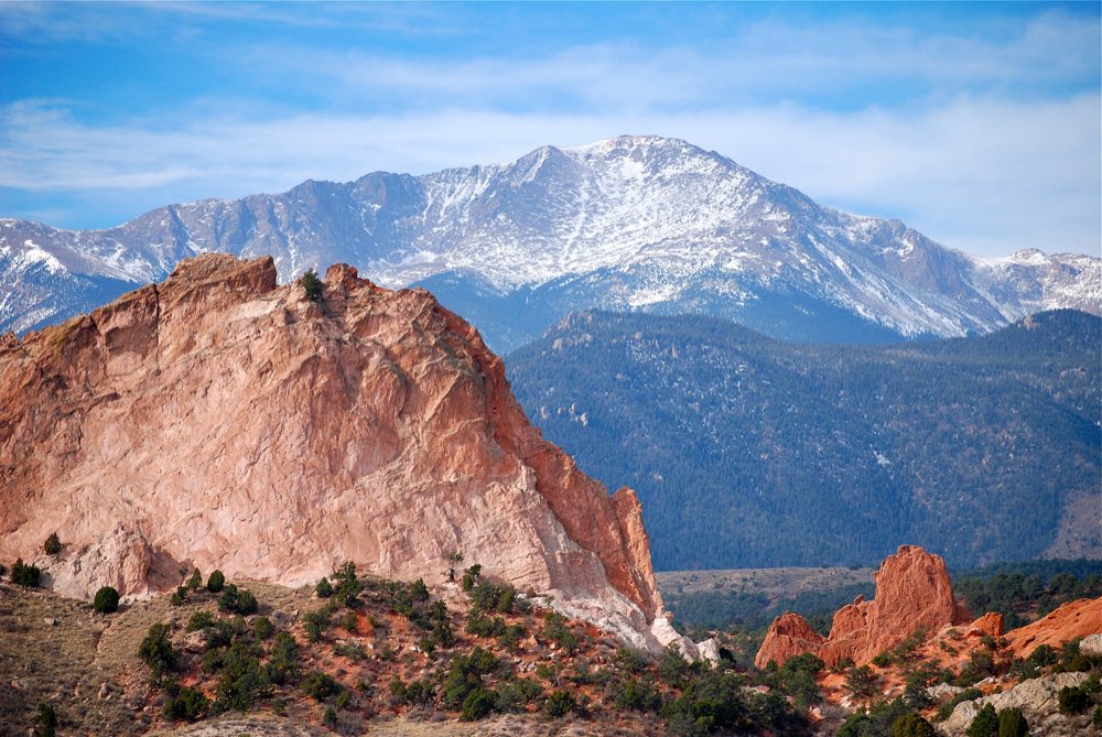 A red sandstone formation in Garden of the Gods in front of the snow-dusted bulk of Pikes Peak under a blue sky