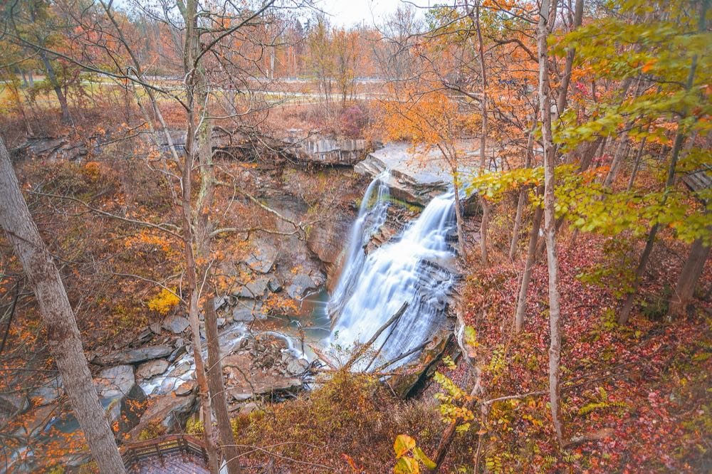 Brandywine Falls spilling over layered rock ledges into a gorge, framed by orange, red and yellow autumn trees