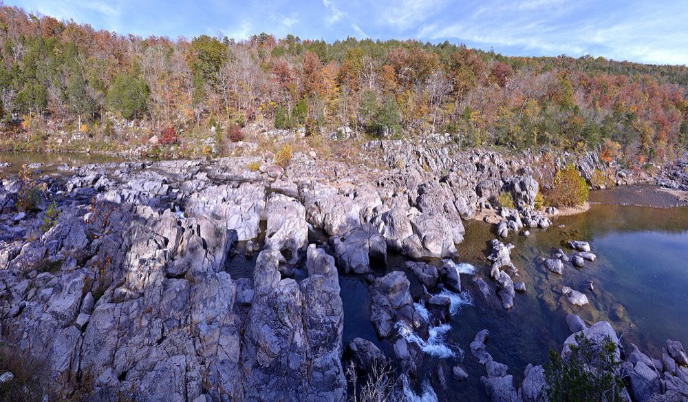The East Fork of the Black River pouring through gray rock chutes and pools at Johnson's Shut-Ins, with a hillside of orange, red and green fall trees behind