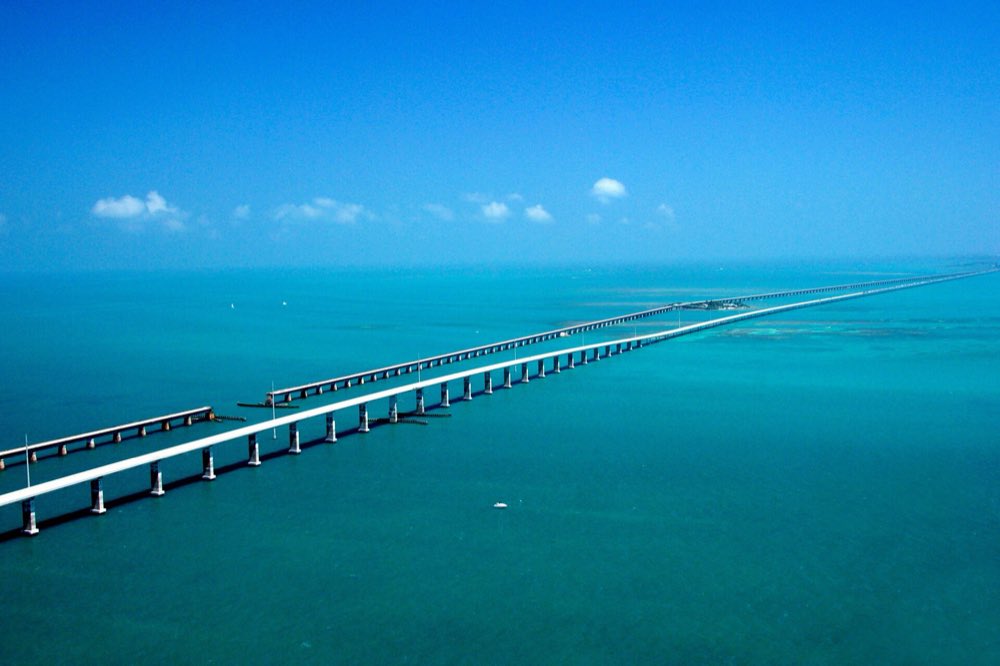 The Seven Mile Bridge seen from the air, running across turquoise water beside the older Flagler railroad bridge under a clear blue sky