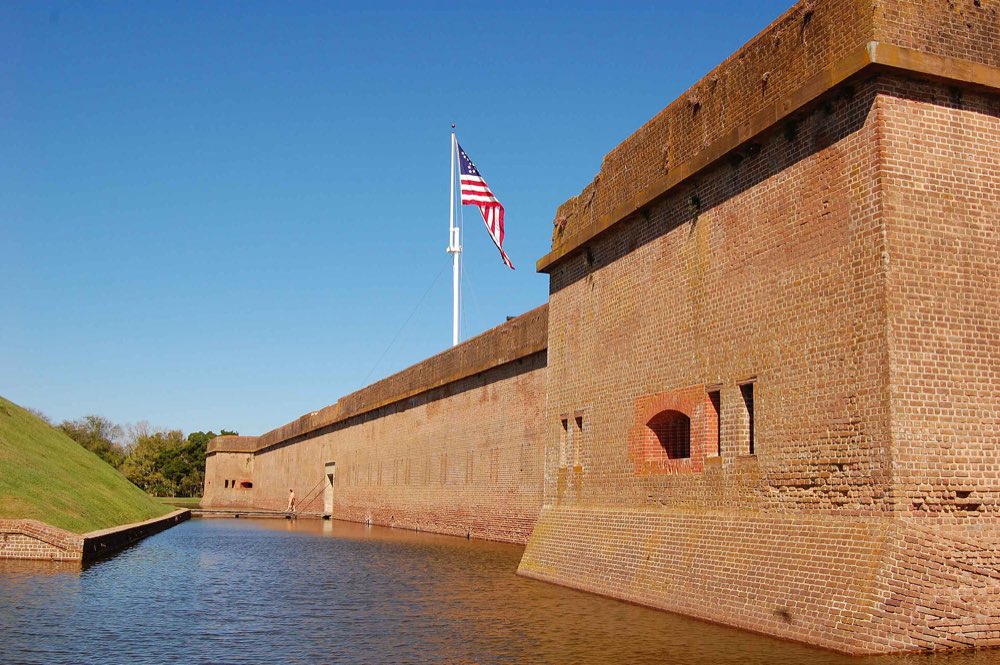 The tall brick walls of Fort Pulaski rising straight from a still green moat, a large American flag flying above the fort under a clear blue sky