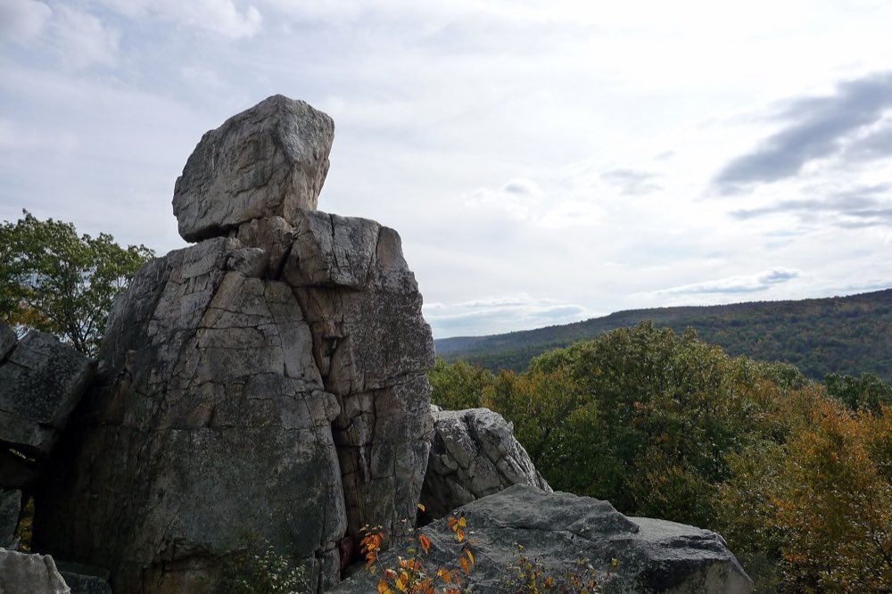 The stacked gray rock column of Chimney Rock above a ridge of orange and green fall trees, with Catoctin's wooded hills rolling away under a soft cloudy sky