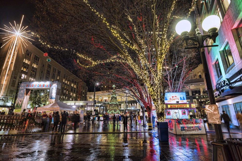 Westlake Park on a wet December night, with lit trees, a lit Christmas tree, a holiday carousel booth and a large light-up star on a building