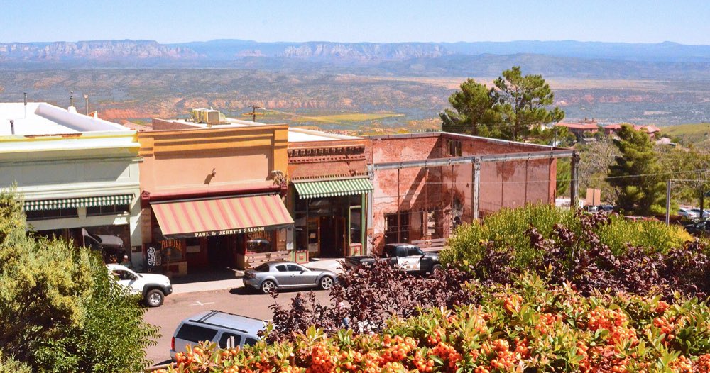 Old brick and stucco storefronts on a Jerome hillside street, with the Verde Valley and distant red-rock cliffs spread out below