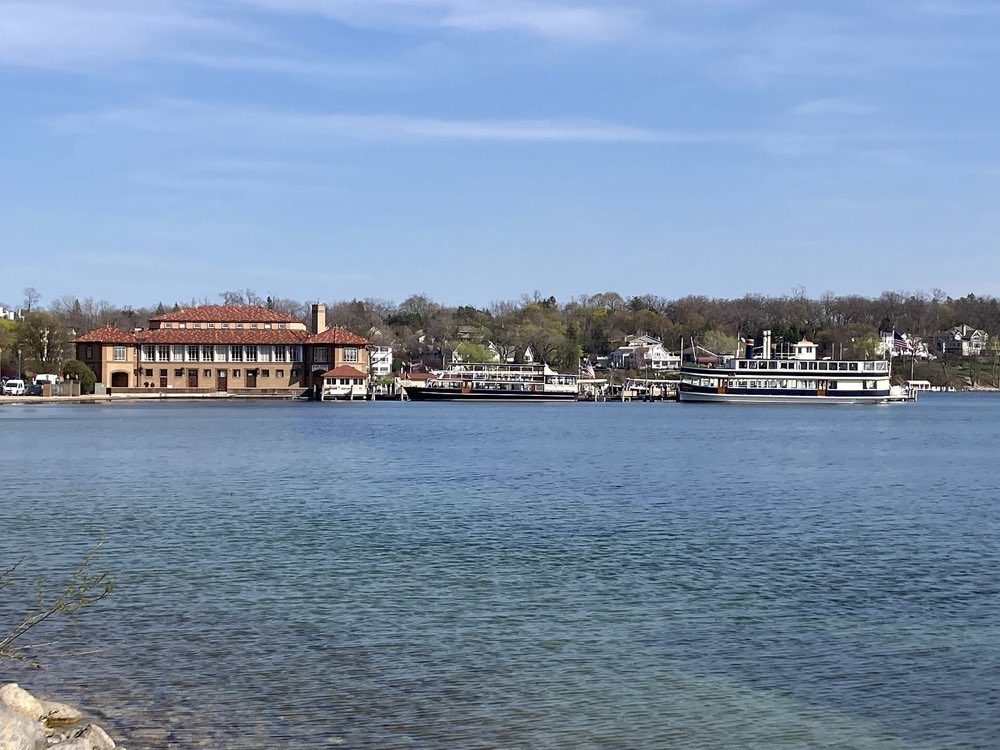 The long tile-roofed Riviera building and tour boats at their docks across a calm blue bay, with wooded shoreline and houses behind