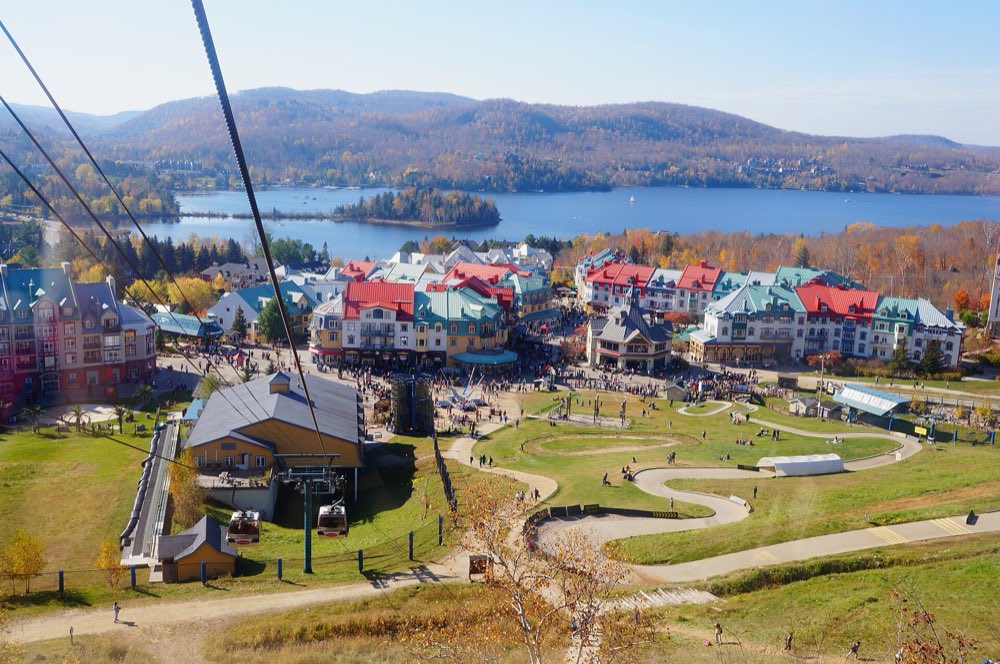 Tremblant's pedestrian village of red, green and blue roofs seen from a lift above the slopes, with Lac Tremblant and autumn-coloured hills beyond