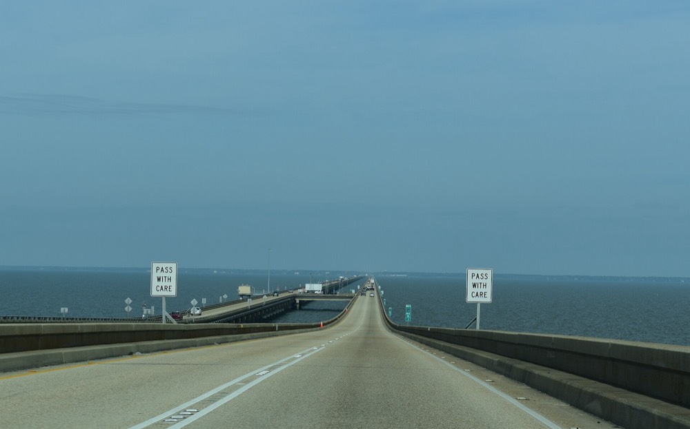 The two-lane Causeway roadway running straight out across gray-blue Lake Pontchartrain toward a faint horizon, with the parallel span and a crossover to the left