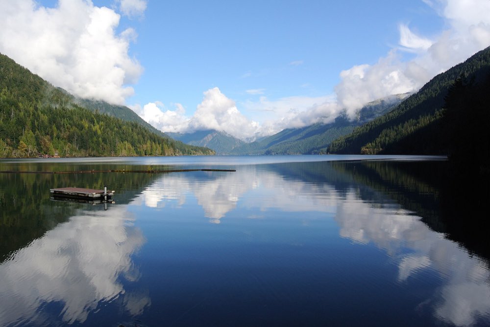 Clouds and forested ridges reflected in the still, clear water of Lake Crescent