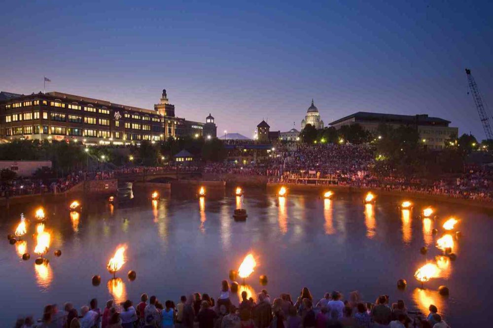 WaterFire at dusk: fires burning in braziers across the Waterplace basin, crowds along the walls, and the lit State House dome and downtown buildings behind