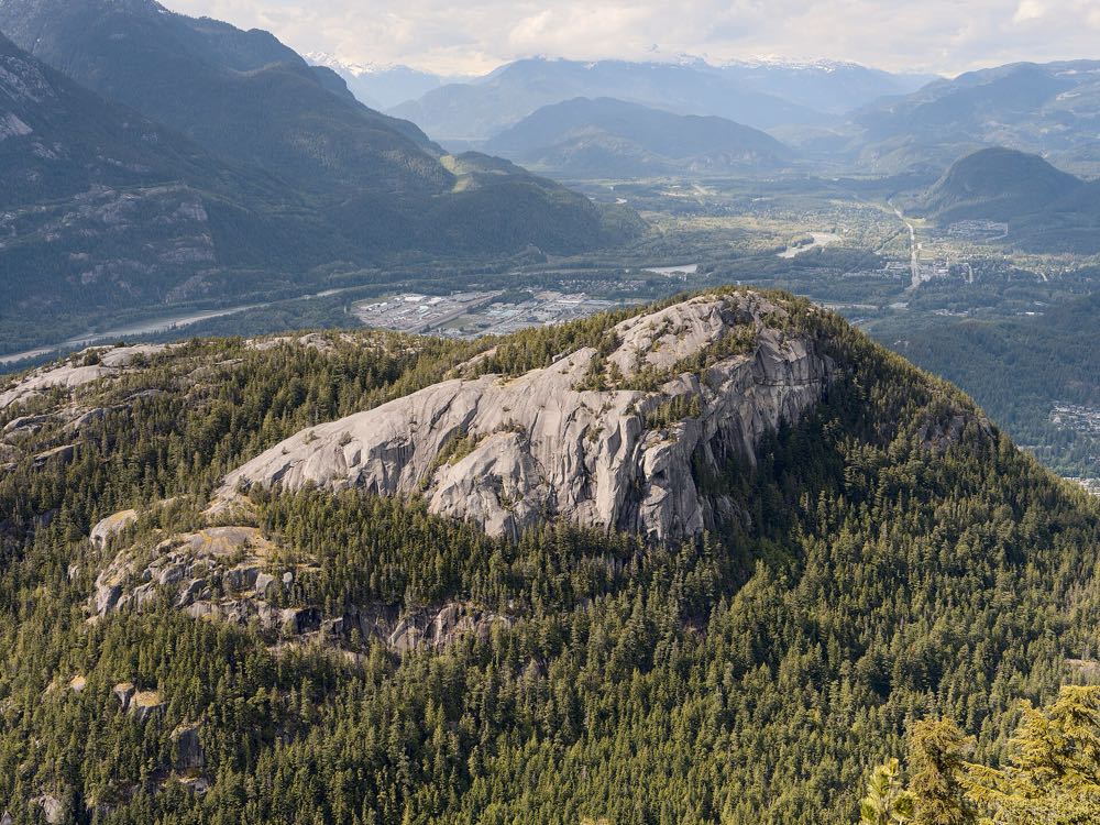 The bare granite dome of the Stawamus Chief rises above dark green forest, with the Squamish valley, river and surrounding mountains spread out behind it
