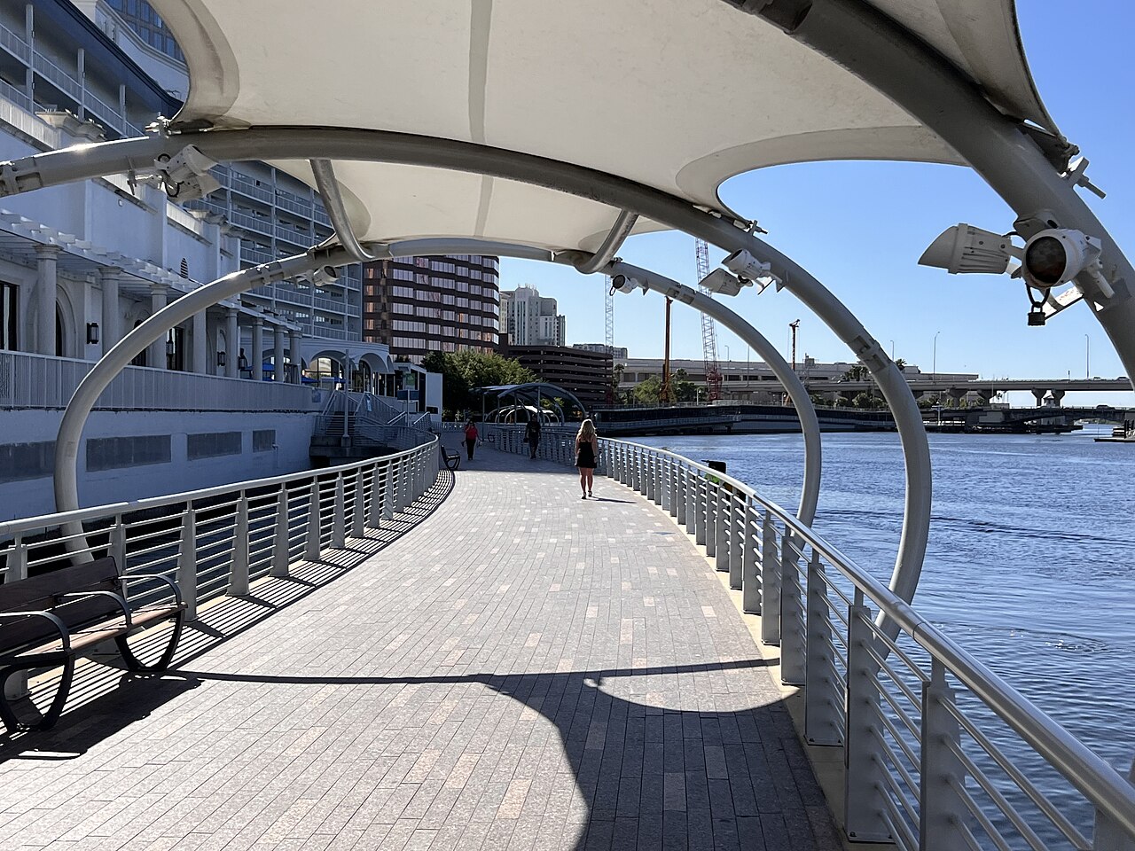 A shaded stretch of the Tampa Riverwalk beside the water in downtown Tampa