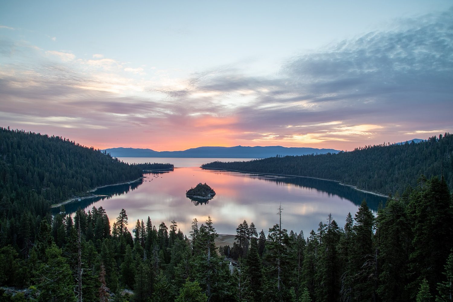 Pink and gold sunrise sky reflected in Emerald Bay at Lake Tahoe, with Fannette Island and pine-covered shores
